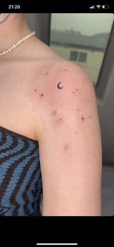 a woman's arm with stars and the moon tattoo on her left shoulder, in front of a window