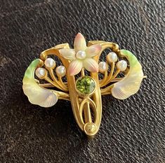 An enchanting Art Nouveau era flower pin by American maker Whiteside & Blank with iridescent enameling and a peridot center.  The soft pink petals remind us of cherry blossoms while the green enameled leaves look like samara seeds!  Wonderfully detailed with pearl accents.  The pin is stamped with the maker's mark along with faded marks for 14K stamps. Metal: 14K Yellow Gold Weight: 6.1 grams Measurement: 1 inch long by 1.1 inches wide Markings: Maker's mark Condition: In very good antique condition with some minor surface wear consistent with age.  One petal may have had the enamel touched up previously. Follow us on Instagram @alphaomegajewelry for the latest updates from our shop!  We have lots of fun there and add videos, highlights, and showcase our newest acquisitions. Art Nouveau Clothing, Art Nouveau Hair, Pink Petals, Enamel Flower, Maker's Mark, Flower Pins, Samara, Cherry Blossoms, Soft Pink