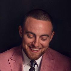 a man in a pink suit smiling and looking at his cell phone while wearing a tie