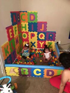 two babies playing in a playpen with letters and numbers