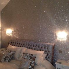 a bed with pillows and lights in a room that has glitter on the wall behind it