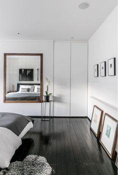 a bedroom with white walls and wood floors has a large mirror on the wall above the bed