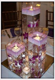 there are many square candles in the center of this table with purple flowers on it