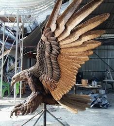 a large wooden sculpture of an eagle on a stand in front of a metal structure