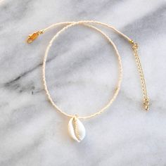 Channel your inner mermaid with this delicate cowrie shell choker. Choose from simple solids or exclusive color mixes for a beach-ready look. glass seed beads genuine cowrie puka shell pendant durable and flexible beading wire gold-plated lobster claw closure, crimps, crimp covers and 2" extension chain lead-free and nickel-free length is approximately 13.5" with a 2" extension chain packaged with a logo kraft card in a clear resealing bag for storage EXCLUSIVE STYLES BLUSH MIX: ivory, cream, bl Beaded Cowrie Shell Beachy Jewelry, Beachy Beaded Cowrie Shell Jewelry, Beachy Cowrie Shell Beaded Jewelry, Beaded Cowrie Shell Strand Jewelry, Adjustable Shell Necklace With Tiny Beads For Beach, Dainty White Shell Necklace, Beach Shell Jewelry With Tiny Beads, Adjustable White Cowrie Shell Choker, White Shell Dainty Jewelry