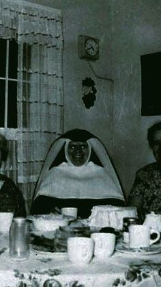 three people sitting at a table with food in front of them and one person wearing a nun costume