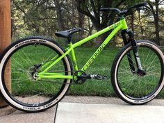 a green bike parked next to a wooden post on the sidewalk in front of some grass