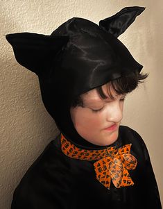 a young boy wearing a black cat costume with an orange bow around his neck and ears