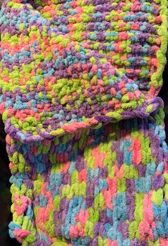 a multicolored crocheted blanket laying on top of a black surface