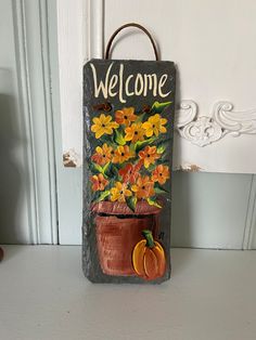 a welcome sign hanging on the side of a door with flowers and pumpkins painted on it