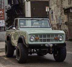 an old green truck parked in front of a brick building on a cobblestone street