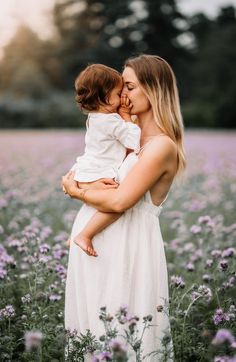 a woman holding a baby in her arms while standing in a field of purple flowers