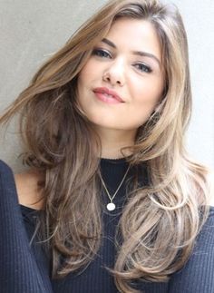 a woman with long brown hair wearing a black top and silver necklace looking at the camera