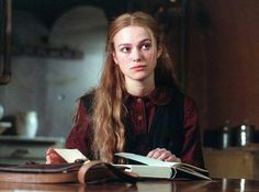 a woman sitting at a table with an open book in front of her and looking off to the side