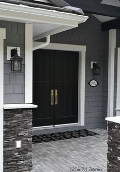 a black front door on a gray house with white trim and brick walkway leading up to it