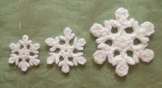 three crocheted snowflakes sitting on top of a green cloth covered table