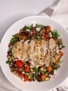 a white bowl filled with chicken and vegetables on top of a table cloth next to a fork