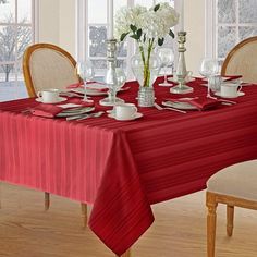 a red table cloth on a dining room table with white flowers in vases and silverware