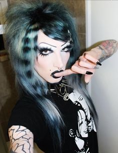 a woman with green hair and piercings holding her finger up to the camera while standing in front of a door