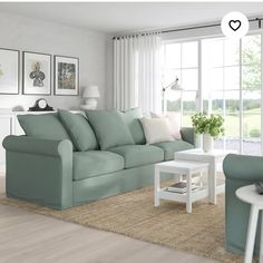 a living room filled with furniture next to a window covered in white curtains and pillows