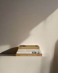 three books sitting on top of each other in front of a white wall with the shadow of a person's hand