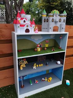 a toy shelf that has some toys on top of it in the grass next to a wooden fence