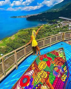 a woman standing on top of a wooden deck next to a large colorful kite in the air