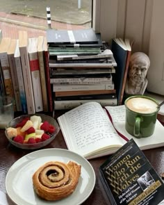 a table topped with books next to a cup of coffee and an apple cinnamon roll