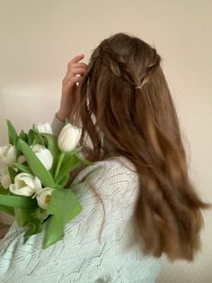 a woman with long hair is holding flowers in her hand and looking at the wall