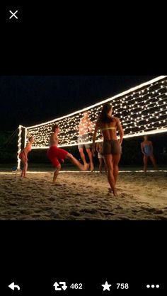 people are playing volleyball on the beach at night with lights strung across the sand and in front of them