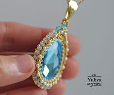 a person holding a necklace with a blue stone in it's center and beading around the edges