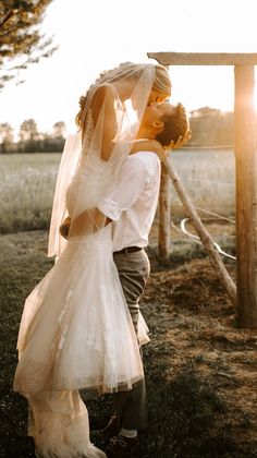 a bride and groom kissing in front of a wooden fence with the sun behind them