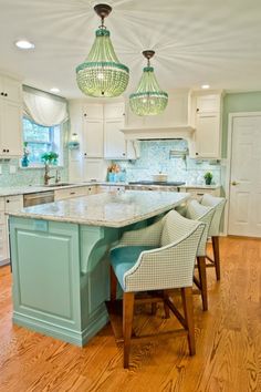 a kitchen with an island and two chandeliers hanging from it's ceiling