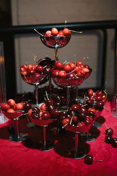 there are many cherries in the glass bowls on the red tablecloth with silver candlesticks