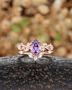 a ring with an amethorate and white diamonds on it sitting on top of a rock