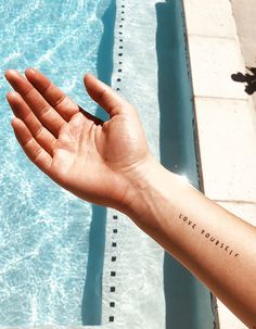 a person's arm with a tattoo saying love yourself in front of a swimming pool