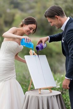 a bride and groom are pouring blue liquid into an easel for their wedding ceremony