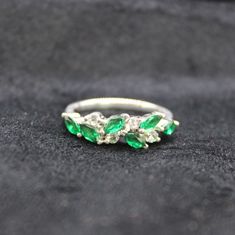 an emerald and diamond ring sitting on top of a black velvet covered surface, with three stones in the middle