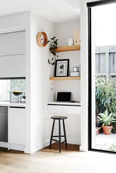 a kitchen with white walls and open shelves on the wall, along with a bar stool