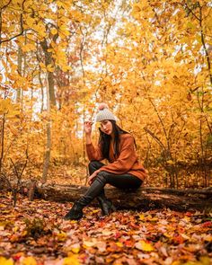 a woman sitting on a log in the woods surrounded by fall leaves and yellow trees