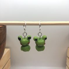 two green frog shaped earrings hanging from hooks