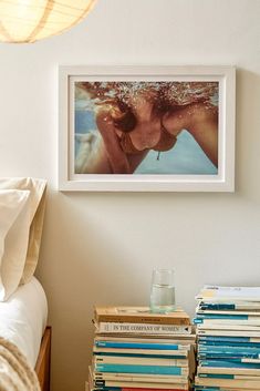 a bed with books stacked on top of each other next to a lamp and framed photograph