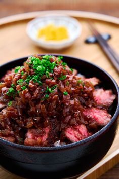 a black bowl filled with meat and green onions