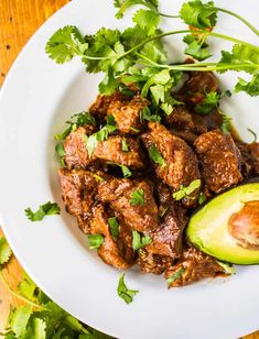 a white plate topped with meat and an avocado next to cilantro