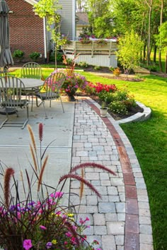 an outdoor patio with chairs and flowers in the foreground, next to a brick walkway