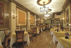 a dining room with tables and chairs covered in yellow tablecloths, chandeliers and pictures on the wall