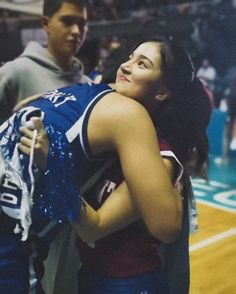 a woman is hugging her friend on the basketball court while another man stands behind her