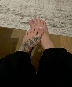 a woman's foot with tattoos on it sitting in front of a wooden floor