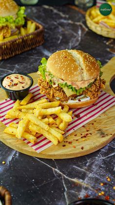 a chicken sandwich and french fries on a cutting board with dipping sauce in the background