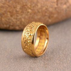 a gold wedding ring with intricate designs on the outside and inside, sitting next to a rock